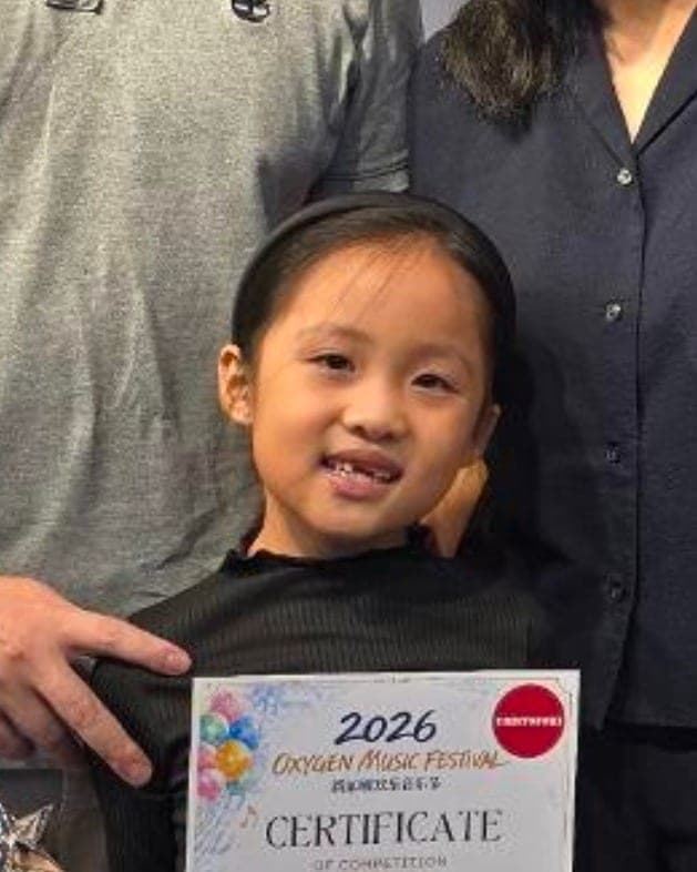 Ellie, seven, receiving her Silver certificate at the Oxygen Music Festival 2026, with her parents standing behind her